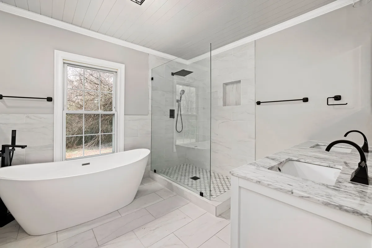 Bright remodeled bathroom with freestanding tub, glass shower, and marble surfaces